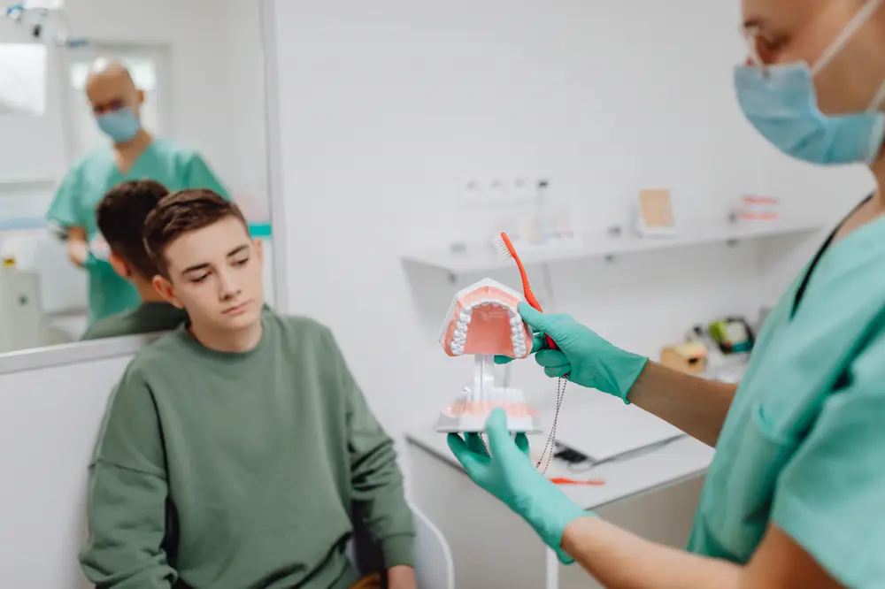 Dental professional showing a teenager how to brush with a tooth model